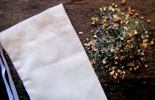 Image of a muslin back with dried herbs and flowers scattered next to it.