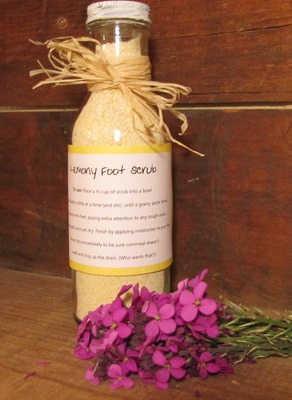 Bottle filled with homemade foot scrub decorated with a raffia bow. Handmade label on the bottle says, "Healing Foot Scrub". A bouquet of violets sits in the foreground.