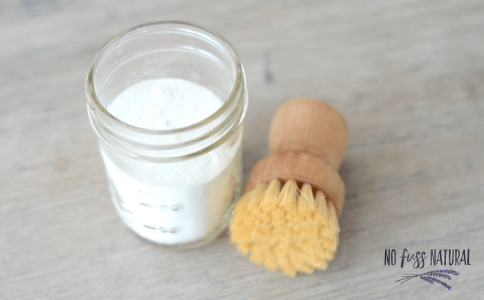 baking soda in glass jar and wooden scrub brush on table for green cleaning