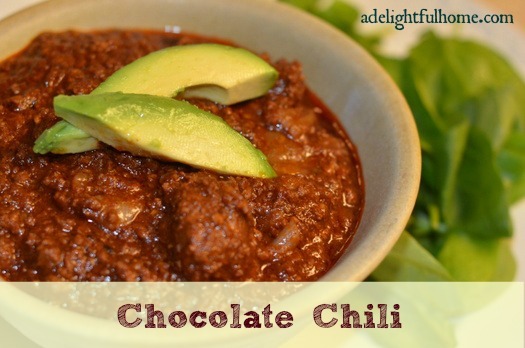 Close up image of a bowl of chili garnished with avocado slices. Text overlay says, "Chocolate Chili".