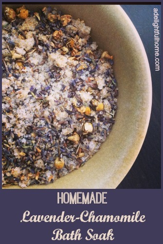 Bird's eye view of chamomile and lavender flowers in a stoneware bowl. Text overlay says, "Homemade Chamomile-Lavender Bath Soak".