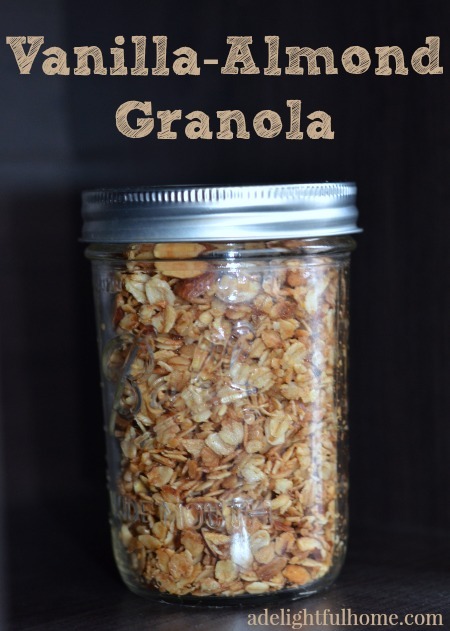 Mason jar filled with homemade granola on a black background. Text overlay says, "Vanilla-Almond Granola".