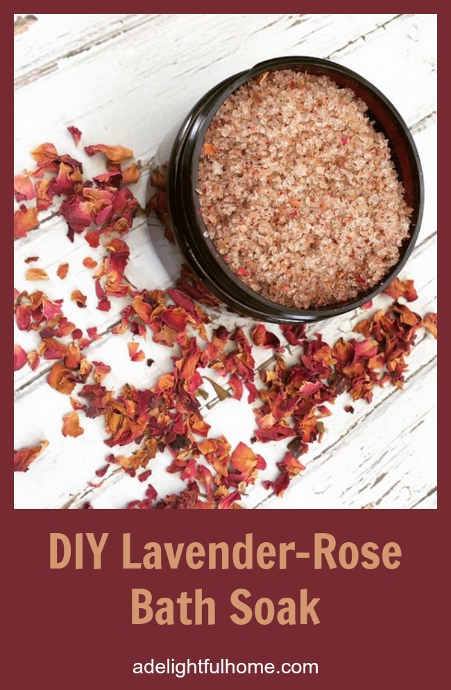 Bird's eye view of an amber glass jar filled with rose colored bath salts. Dried rose petals are scattered around for decorative effect. Text overlay says, "DIY Lavender-Rose Bath Soak".