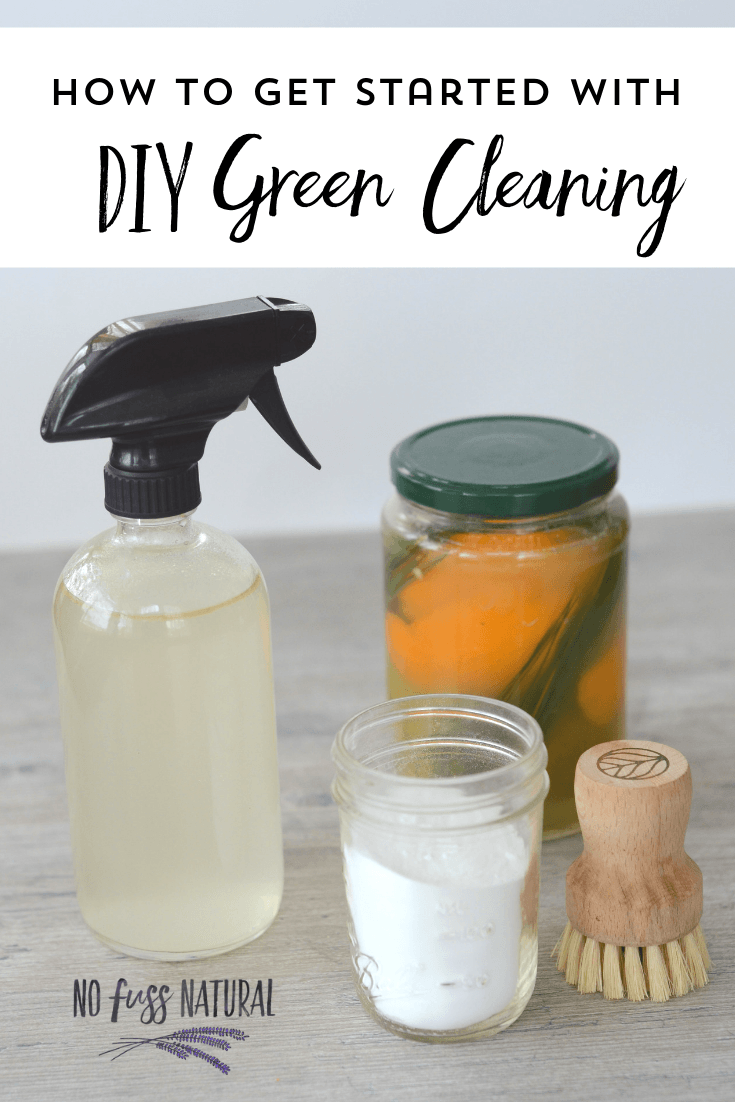 collection of DIY green cleaning supplies: glass spray bottle with homemade cleaner, fruit peel vinegar in jar, baking soda in jar, and wooden scrubbing brush