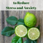 A bird's eye view of fresh bergamot fruit and leaves on a natural wood surface. Text overlay says, "How to Use Bergamot Essential Oil to Reduce Stress and Anxiety".