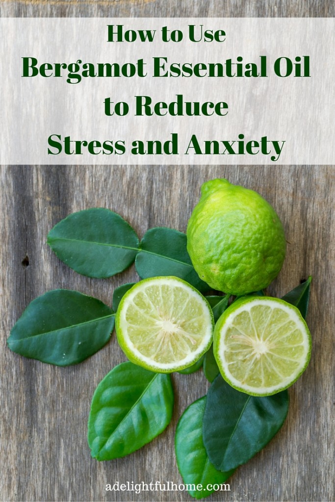 A bird's eye view of fresh bergamot fruit and leaves on a natural wood surface. Text overlay says, "How to Use Bergamot Essential Oil to Reduce Stress and Anxiety".