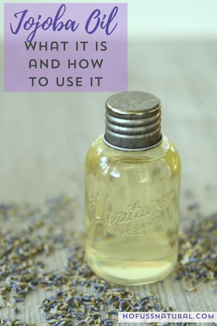 A glass bottle filled with jojoba oil with lavender sprigs scattered in the background. Text overlay says, "Jojoba Oil - What it is, and How to Use it".