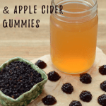 Image of a jar full of apple cider vinegar sitting next to a ramekin filled with gummies. More gummies are scattered between the two. Text overlay says, "Homemade Elderberry and Apple Cider Vinegar Gummies".