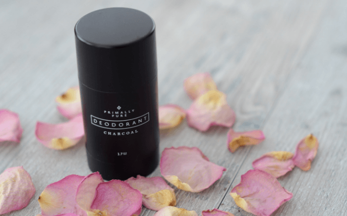 Container of natural charcoal deodorant with rose petals strew around it